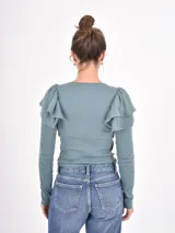 Remera de manga larga en color beige, confeccionada en tejido acanalado, con cuello redondo y detalle de volados en los hombros.