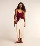 Pollera midi color crudo confeccionada en sarga de algodón, con cintura con trabillas, cierre con botón y cremallera, bolsillos y abertura frontal.