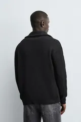 Chaqueta de punto con textura acanalada, cuello subido y cierre frontal completo con cremallera metálica. Presenta un corte relajado y acabados en rib en puños y ruedo.