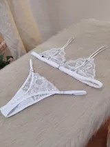 Conjunto de lencería compuesto por un bralette triangular de encaje floral con breteles regulables y una bombacha tipo tanga a juego con detalles de encaje y tiras ajustables.
