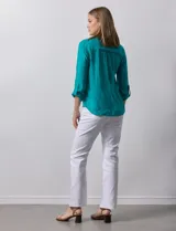 Blusa blanca de gasa marca Zac & Rachel, con cuello a la base, escote en V, abertura central con botones, bolsillo aplicado en el pecho y mangas largas regulables con presilla y botón. Tiene terminación opcional de nudo en el ruedo.