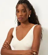 Blusa sin mangas de punto acanalado color crema, con escote en V y espalda descubierta. Confeccionada en una mezcla de viscosa y poliamida, presenta un ajuste al cuerpo y textura vertical en relieve.