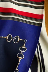 Pollera larga con diseño cruzado efecto pañuelo y brillo sutil. Presenta un estampado geométrico multicolor en tonos azul, rojo y crudo con detalles de cadenas.