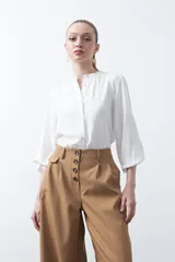 Camisa de color celeste claro con silueta relajada y mangas largas. Presenta un cuello redondo con pequeña abertura frontal y botones, además de un delicado trabajo de tablas en los hombros que aporta textura al diseño.