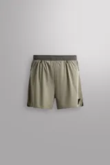 Pantalón corto de trail running color beige, confeccionado en tejidos técnicos ligeros y elásticos. Cuenta con forro interior, cintura elástica ajustable con cordón, bolsillos traseros laterales multifunción, bolsillo trasero central con cremallera, bajo con costura termofijada y aberturas laterales. Incluye logo estampado en la pernera.