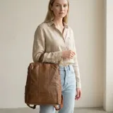 Mochila urbana de eco-cuero marrón tostado, de diseño estructurado con bolsillos laterales y asa superior.