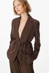 Blazer de corte entallado color marrón chocolate, con solapas clásicas, cierre frontal con un botón y un lazo fino integrado en la cintura para ajustar la silueta.