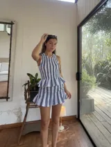 Top sin mangas confeccionado en lino, con diseño de nido de abeja en el torso y detalle de volado en el ruedo. Presenta patrón de rayas verticales en tonos azul y blanco.