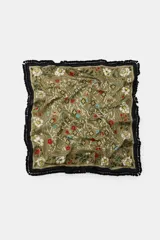 Pañuelo cuadrado de algodón con estampado floral y geométrico sobre fondo verde oliva. Presenta un borde negro con flecos decorativos en todo su contorno.