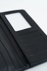 Billetera negra de textura granulada con cierre de solapa y botón a presión metálico. Incluye una correa de muñeca extraíble.