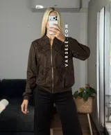 Campera tipo bomber confeccionada en gamuza, con cierre frontal metálico y detalle de flores bordadas en relieve en el frente.