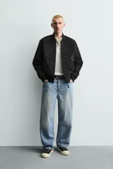 Cazadora bomber ligera de tejido técnico color verde oliva, con cuello, puños y bajo en rib elástico. Presenta cierre frontal de cremallera y bolsillos de vivo en la cadera.