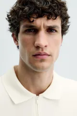 Polo de manga corta color blanco roto, con cuello solapa y cierre frontal de cremallera. Presenta un tejido de piqué estructurado y corte regular fit.
