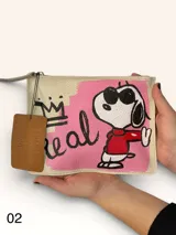 Sobre de cuero marrón con diseño pintado a mano que presenta al personaje Snoopy sobre un fondo rosado y la palabra 'heal'. Cuenta con cierre superior y etiqueta de cuero colgante.
