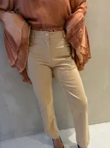 Pantalón sastrero de tiro alto color beige, de corte recto y calce impecable. Presenta detalles de costuras pespunteadas a lo largo de las piernas y pliegues decorativos en los laterales de la cintura.