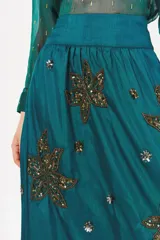 Falda larga color turquesa con cintura alta y apliques bordados de lentejuelas doradas y plateadas en forma de hojas o flores.