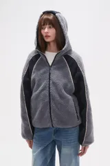 Campera de abrigo de tejido polar (tipo sherpa) color gris oscuro, con capucha y cierre frontal. Presenta paneles de color negro en los hombros y mangas, ribeteados con un vivo de color claro.