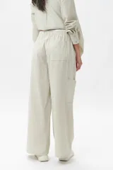 Pantalón de corte amplio y estilo piyamero, confeccionado en algodón con estampado de rayas verticales finas en color verde y blanco. Cuenta con cintura elástica y múltiples bolsillos laterales.