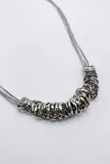 Collar plateado de doble cadena fina tipo serpiente con un conjunto de múltiples aros metálicos entrelazados en la parte central. Cuenta con cadena de alargue y cierre de mosquetón.