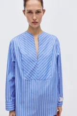 Camisa de algodón con diseño a rayas azules y blancas, corte oversized, escote en V profundo y mangas largas con hombros caídos y puños anchos.