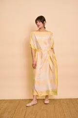 Vestido tipo túnica midi de satén de seda, color amarillo y blanco con estampado toile de Jouy y detalles de guardas tipo pañuelo. Cuenta con escote bote, mangas cortas amplias y lazo ajustable en la cintura.