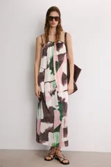 Vestido midi de corte holgado con cuello halter ajustable mediante lazada y hombros descubiertos. Presenta un diseño con tiras cruzadas en la espalda y un estampado abstracto en tonos rosado, verde y marrón sobre fondo blanco.