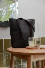 Cartera tipo tote bag de cuero marrón, con diseño minimalista, asas largas y detalles de remaches metálicos en la unión de las asas.