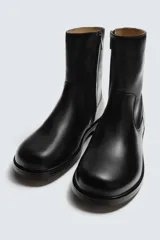 Bota de caña media fabricada en piel color marrón oscuro, con cierre de cremallera lateral, horma cuadrada y suela con ligero tacón.