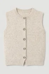 Chaleco tejido de punto en color beige, con cuello redondo y cierre frontal mediante botones decorativos con apliques de cristal.