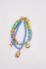 Brazalete multicapa compuesto por cuentas de cristal en tonos azul, verde, amarillo, naranja y transparente. Incluye dijes metálicos dorados con formas de estrella de mar y caracoles marinos.
