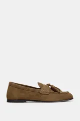 Mocasín de mujer confeccionado en serraje color marrón, con detalle de antifaz y borlas en el empeine. Presenta punta redonda y suela plana.