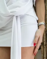 Vestido corto blanco con escote pronunciado en V, mangas cortas tipo murciélago y talle fruncido con un lazo que cae a un lado.