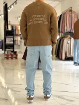 Sweater de punto color marrón, de manga larga, con textura acanalada y texto bordado en la espalda.