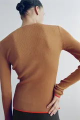 Chaqueta de punto marrón con cuello redondo, manga larga y ribetes en color rojo. Cuenta con cierre frontal de botones.