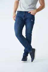 Pantalón de jean corte regular, color azul oscuro, con diseño de cinco bolsillos, pasacintos y detalles de roturas localizadas en la parte frontal.