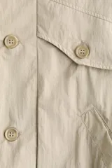Camisa cargo sin mangas de nylon color beige, con cuello alto, cierre frontal de botones, bolsillos superiores con solapa y bolsillos delanteros diagonales. Cuenta con elástico oculto en el bajo.