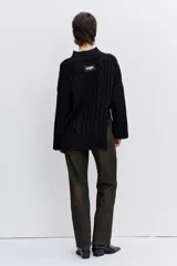 Sweater de punto con diseño de trenzas, cuello alto y mangas largas con puños acampanados. Presenta un corte holgado con terminación asimétrica en el ruedo.