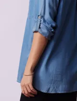 Camisa celeste de tencel con cuello con solapa, abertura central con botones ocultos, bolsillos delanteros y mangas largas regulables con presilla y botón.