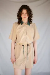 Vestido corto verde militar de microfibra con cuello camisero negro, cintura elastizada con cordón de ajuste y mangas cortas con dobladillo. Cierre frontal con botones.