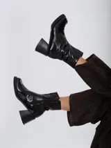 Botas de caña media con acabado charolado brillante, punta cuadrada y taco bloque. Cuentan con cierre lateral interno para facilitar su colocación.