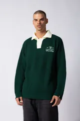 Sweater de tejido tipo waffle en color verde oscuro, con cuello polo en color crema y cierre frontal con botones. Presenta un bordado decorativo en el pecho y un corte relajado.