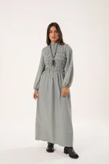 Vestido largo de rayas verticales en tonos gris y blanco, con cuello alto fruncido, mangas largas tipo globo con puños elásticos y cuerpo con diseño de nido de abeja hasta la cintura. Presenta una falda amplia con caída fluida.