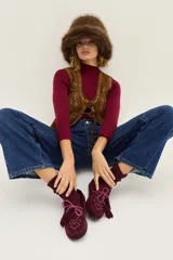 Mocasín de gamuza color bordó con detalle de flecos, cordones y tachas metálicas en la parte superior.