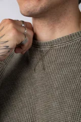 Buzo de corte oversize confeccionado en tela waffle de algodón con proceso de teñido acid wash. Presenta cuello redondo con detalle de costura en X y mangas largas con puños acanalados.