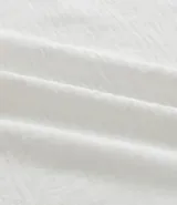 Blusa de manga corta color beige, confeccionada en tela texturizada. Presenta cuello redondo con detalle de pespuntes y cierre trasero con botón en forma de lágrima.