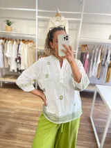 Blusa blanca de manga 3/4 con bordados en hilo verde oliva, cuello mao con abertura y botones, y terminación bordada en el ruedo y puños.