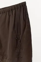 Pantalón de tiro medio y pernera recta, confeccionado en tejido de viscosa semitransparente. Presenta cintura elástica ajustable con cordón, bolsillos laterales y un diseño decorado con bordados a tono y aplicaciones de abalorios.