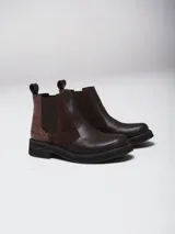 Botinetas tipo Chelsea de cuero marrón, con paneles laterales elásticos y detalle de textura símil reptil en el talón. Poseen suela plana de goma negra con plataforma baja.