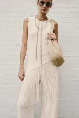 Top confeccionado en hilatura con mezcla de algodón, de cuello redondo y manga sisa, con detalle de aplicación de flecos combinados a tono y bajo asimétrico.