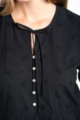 Blusa negra de algodón con diseño de broderie, mangas tres cuartos abullonadas, cierre frontal con botones y detalle de cordón ajustable en la cintura.